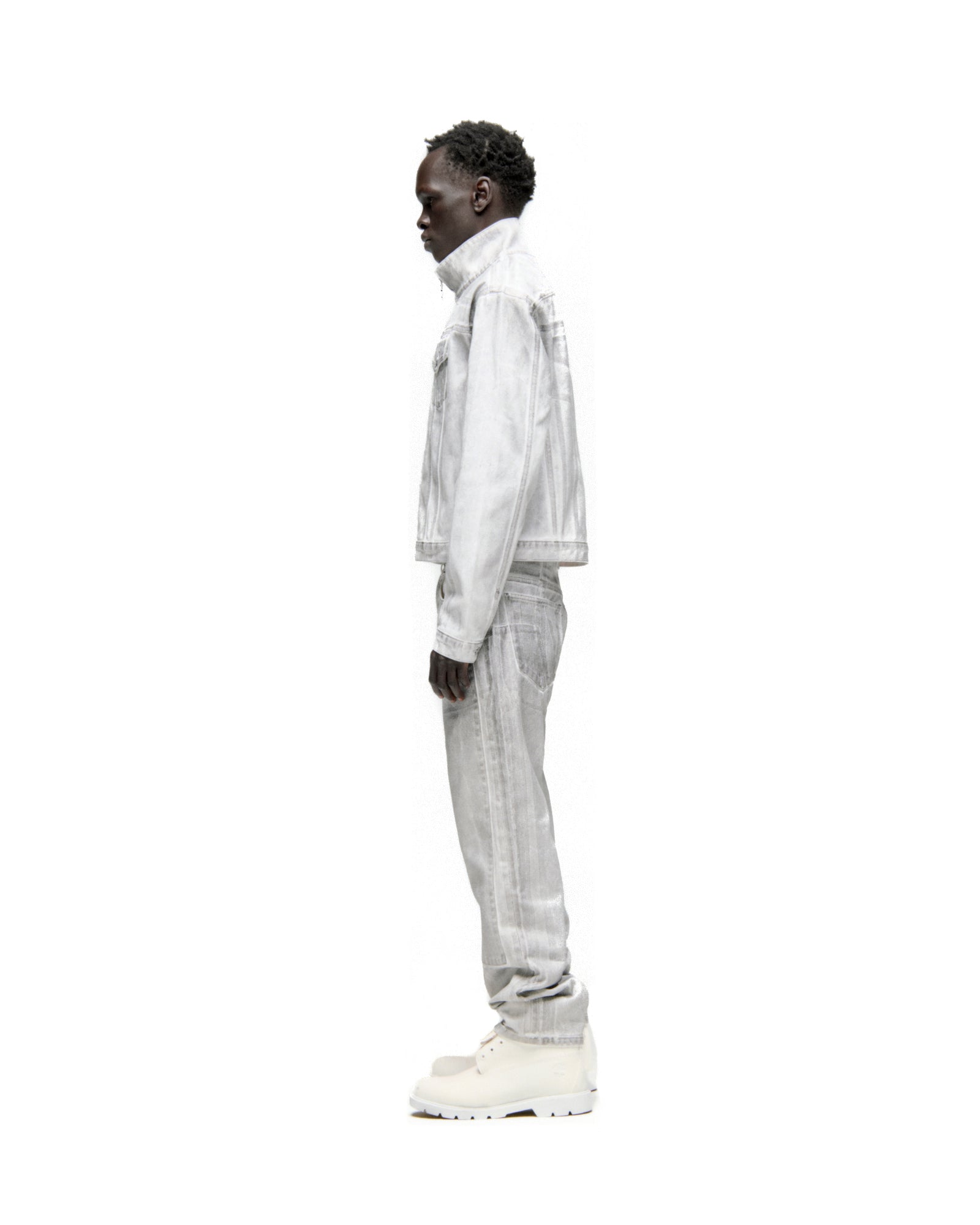 Side view of a man wearing a platinum spray-effect denim trucker jacket and matching jeans.