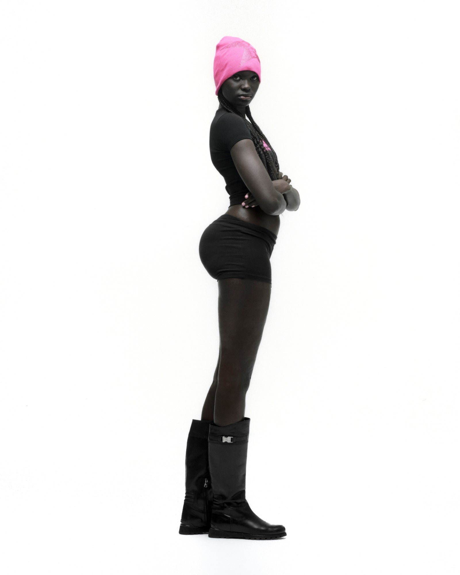 Woman in black cropped MOTO 5 BABY TEE with graphic print, black shorts, and black boots, wearing a pink beanie.