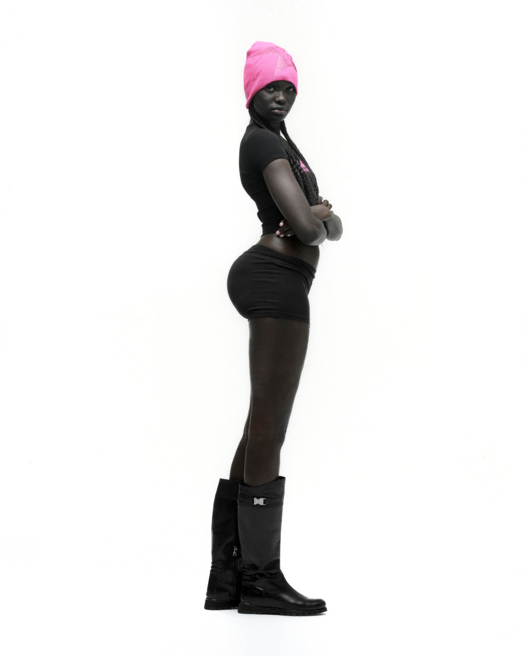 Woman in black cropped MOTO 5 BABY TEE with graphic print, black shorts, and black boots, wearing a pink beanie.