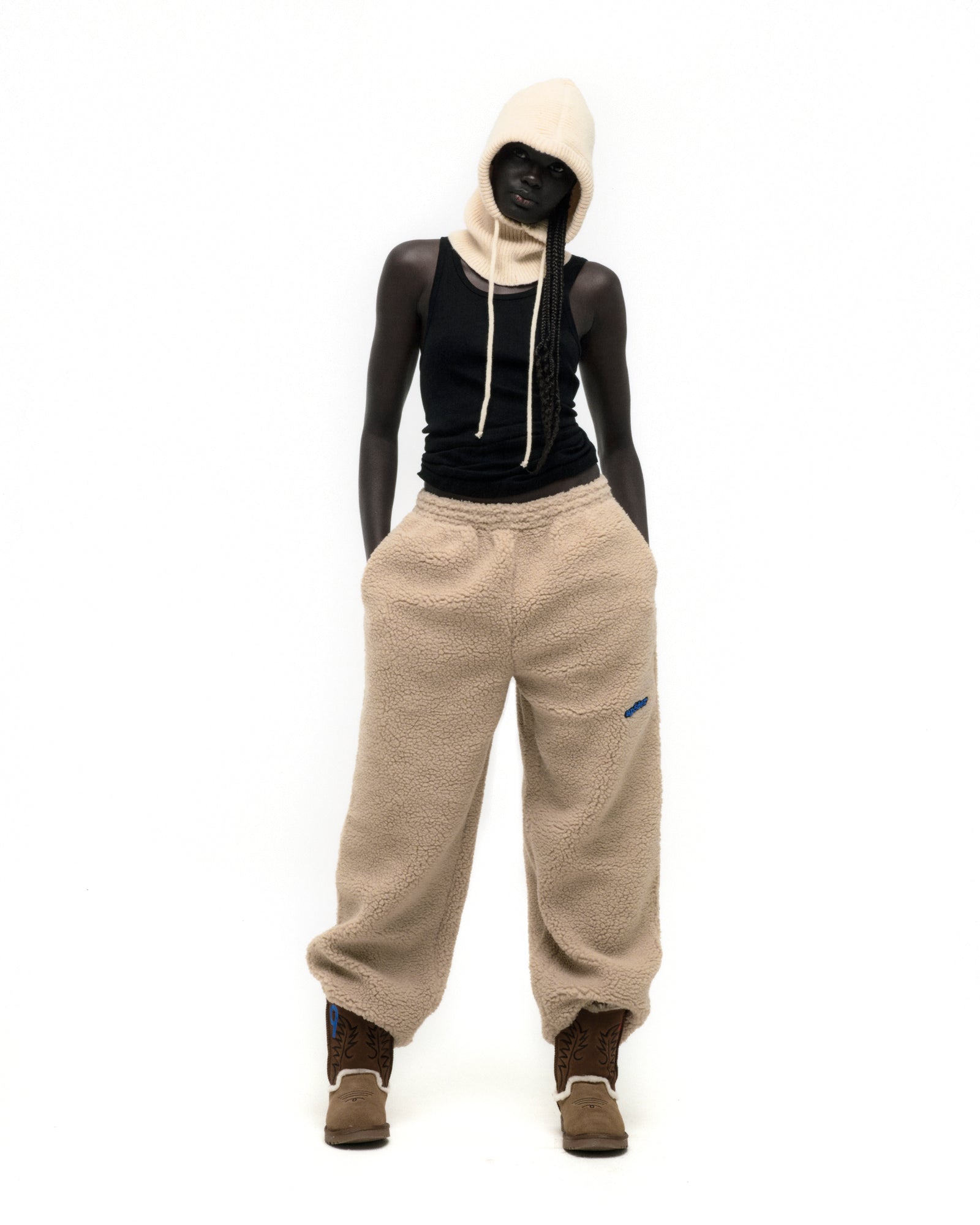 Model wearing beige TEDDY FLEECE PANT, a sherpa fleece pant with a rubberized logo patch.