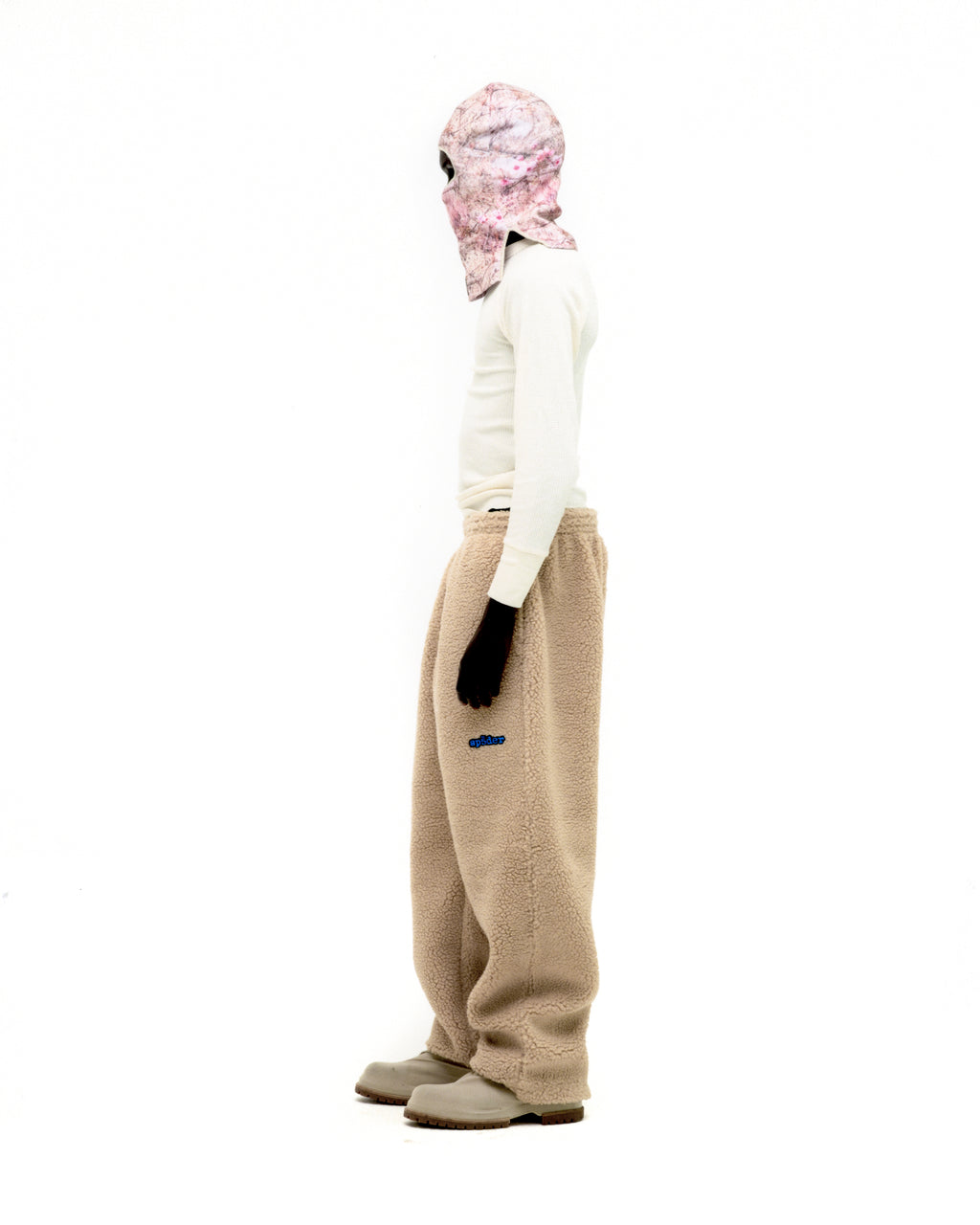 Teddy fleece pant in beige sherpa with blue rubberized logo patch, worn by a person in a white long-sleeve shirt.