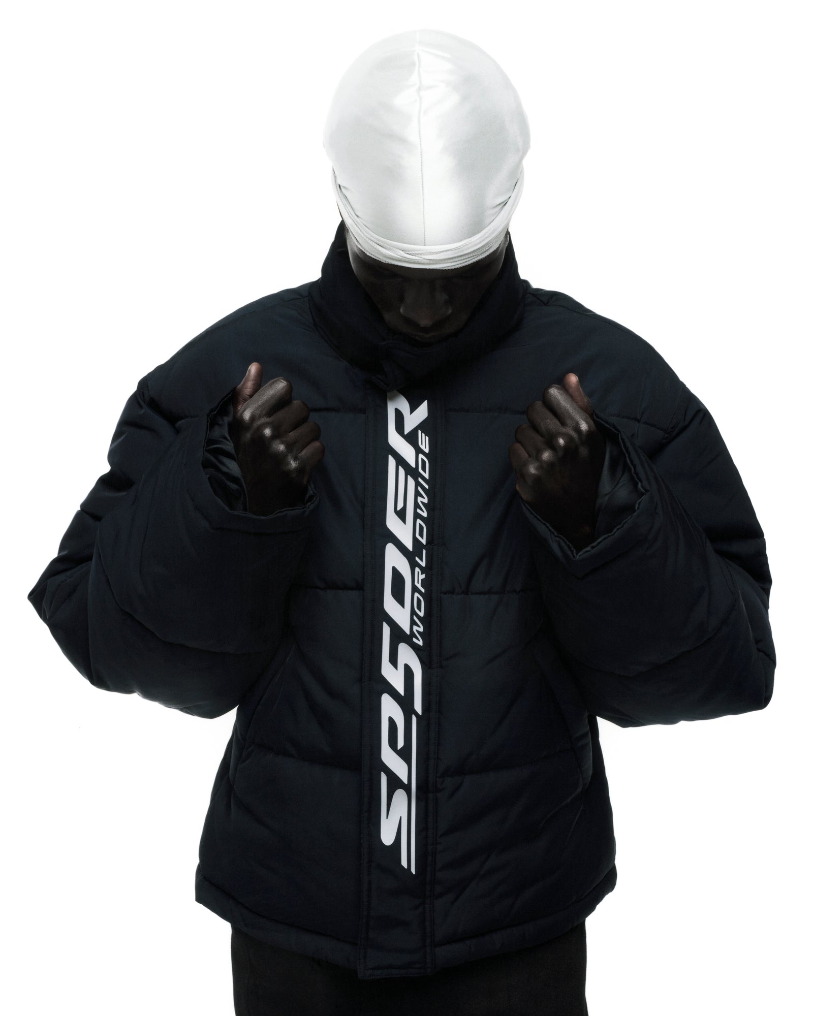 Black poly-fill TRACKHAWK puffer jacket with reflective "SP5DER WORLDWIDE" text graphic along front zip.