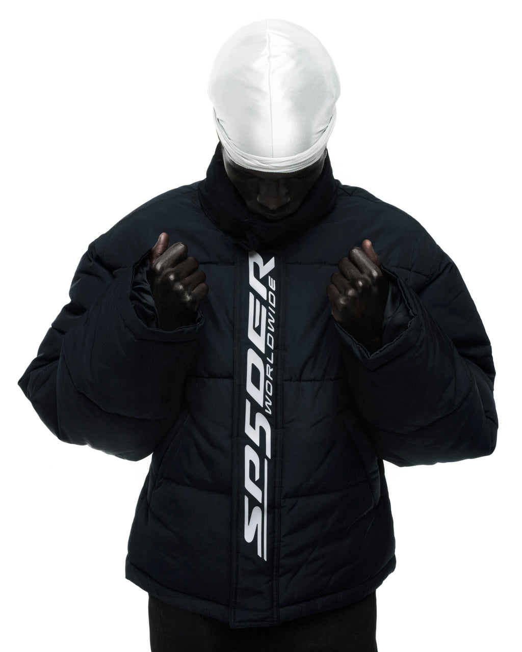 Black poly-fill TRACKHAWK puffer jacket with reflective "SP5DER WORLDWIDE" text graphic along front zip.
