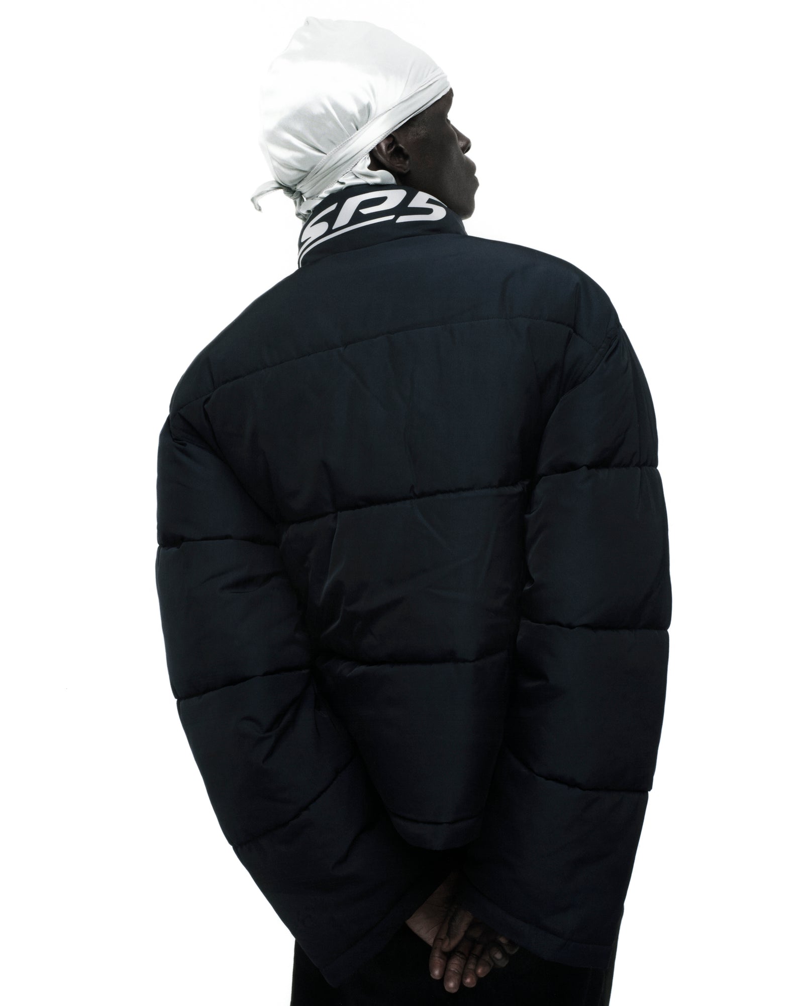 Black TRACKHAWK puffer jacket with reflective text graphic on collar, seen from behind.