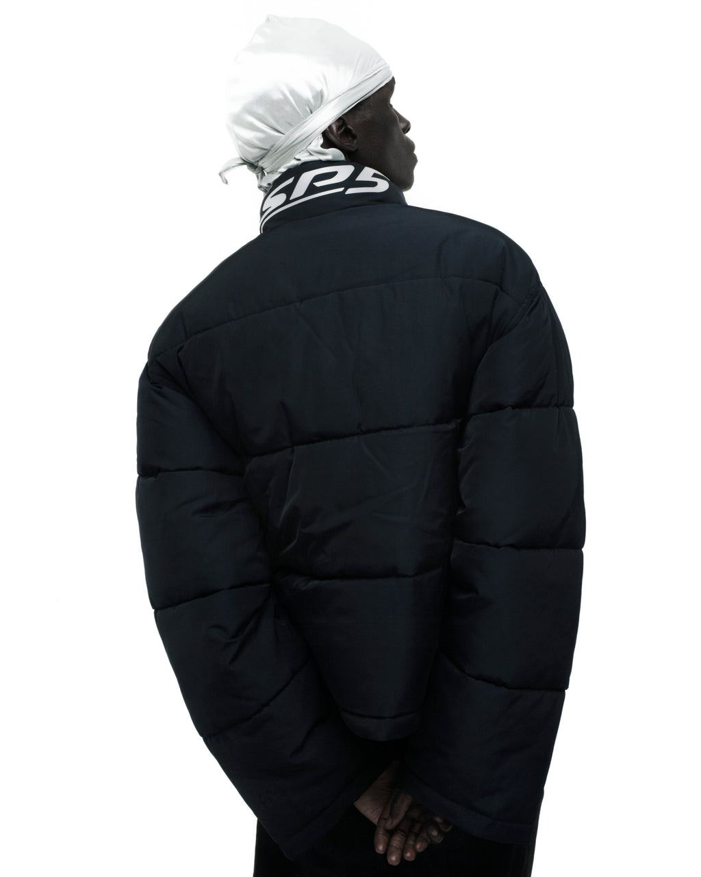 Black TRACKHAWK puffer jacket with reflective text graphic on collar, seen from behind.