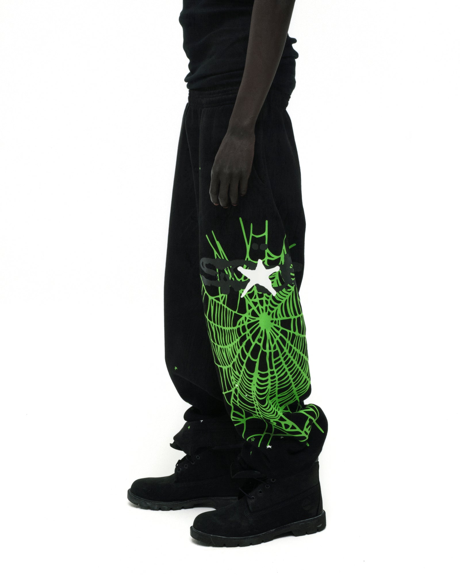 Black cotton fleece sweatpants with a large neon green SP5DER web graphic and scattered stars on the leg.