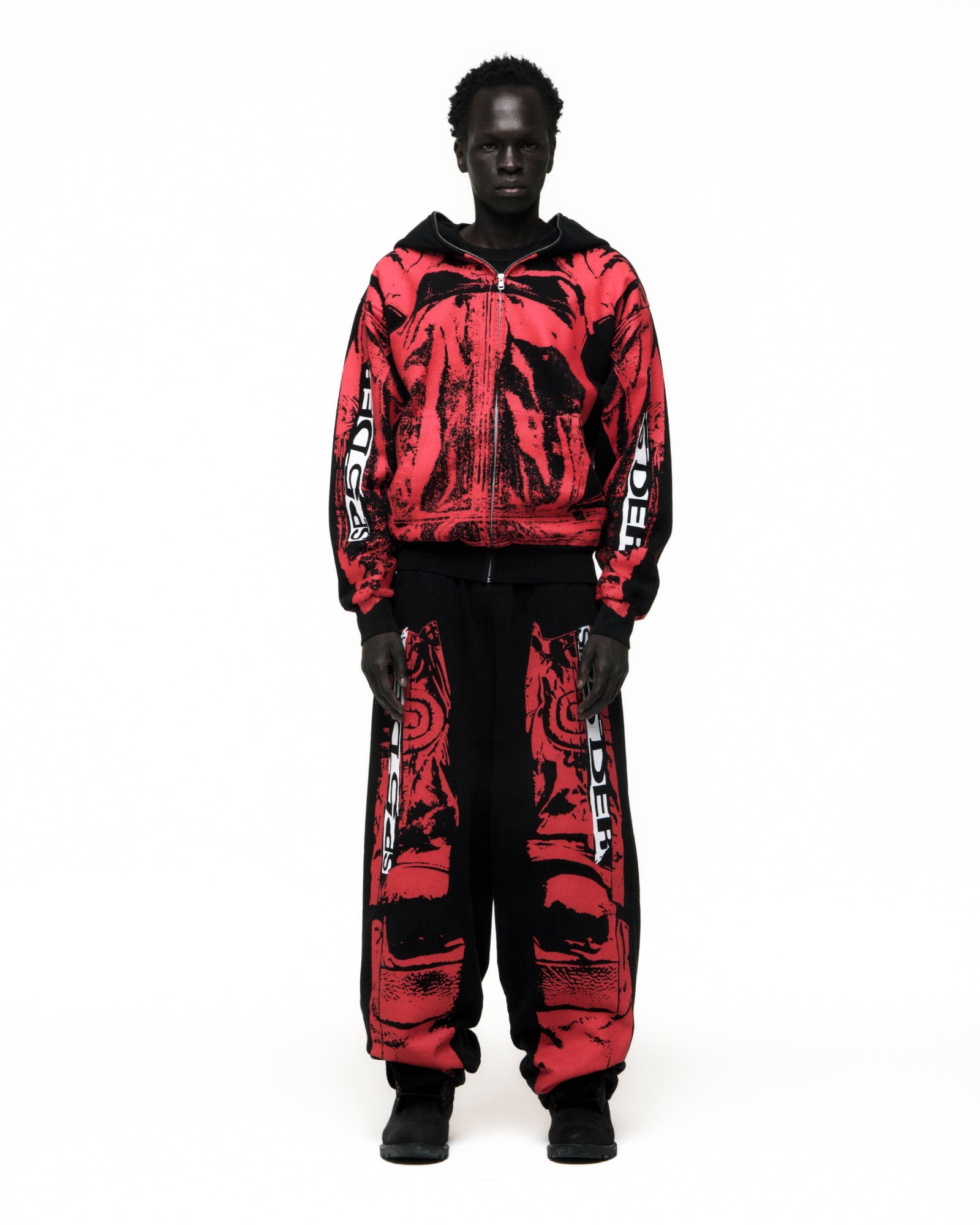 Black model wearing a red and black JP5 Moto Hoodie with painted design, full zipper, and matching pants.