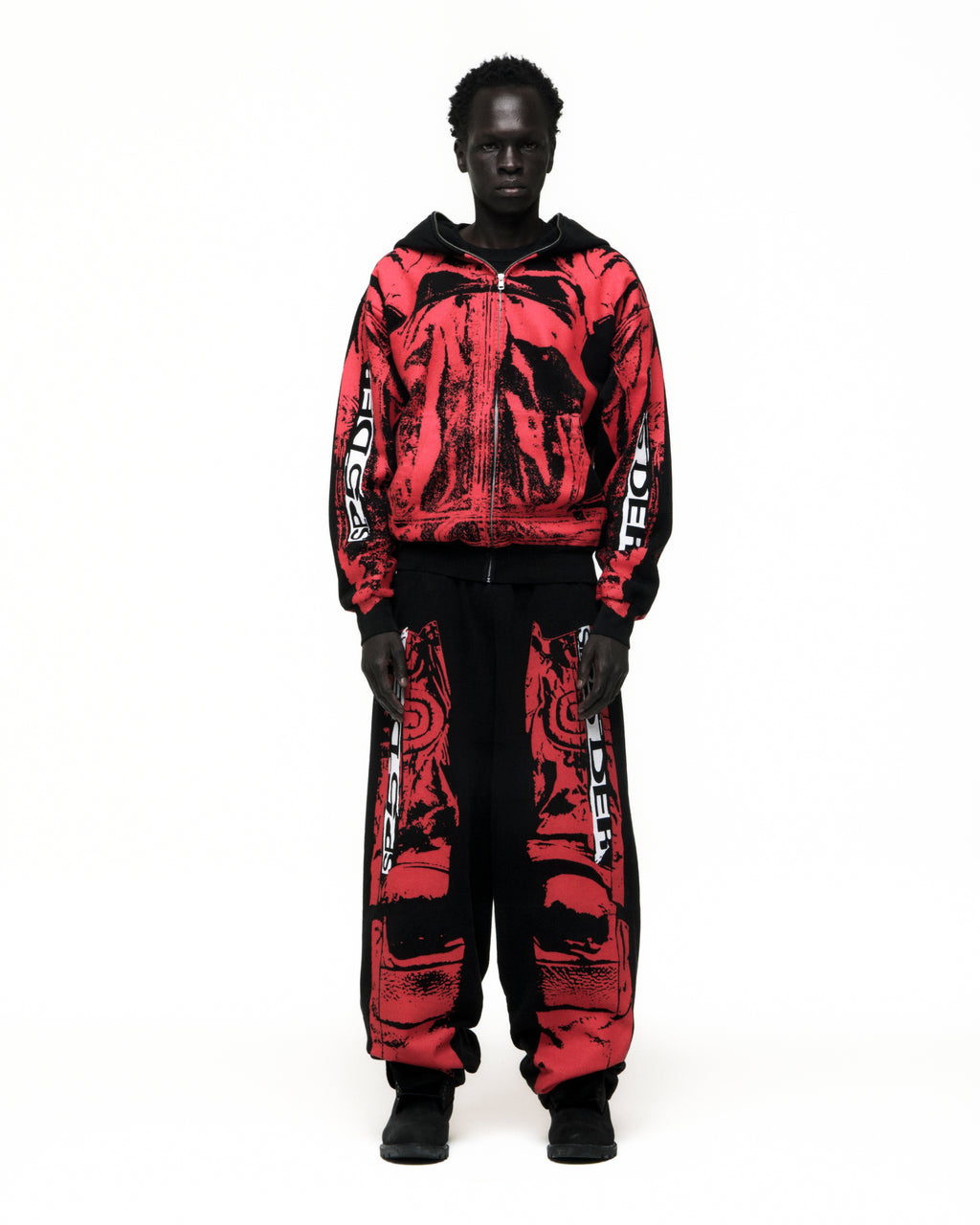 Black model wearing a red and black JP5 Moto Hoodie with painted design, full zipper, and matching pants.