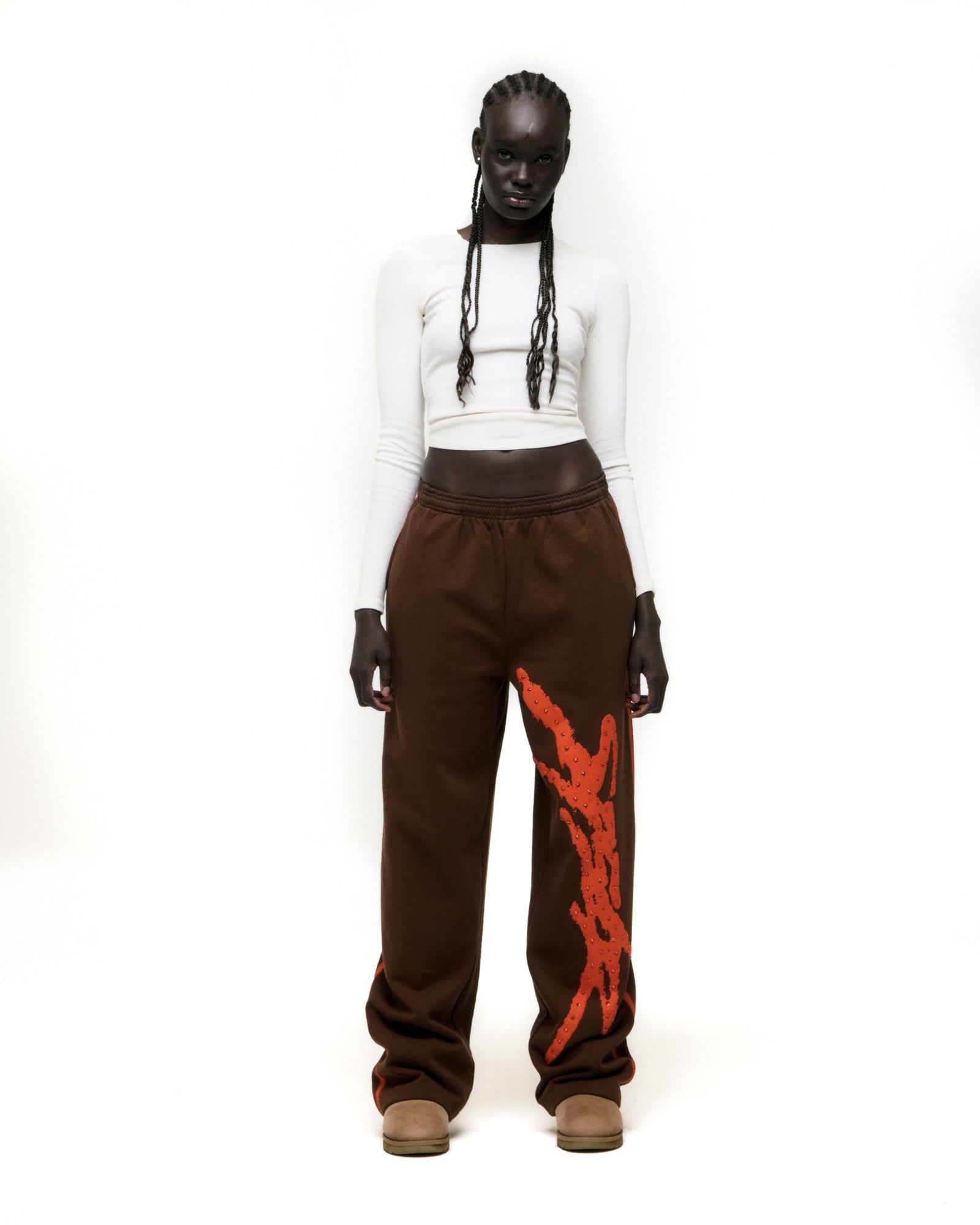 Brown cotton fleece wide-leg sweatpants with orange rhinestone "SP5DER" logo and sprayed side stripe.