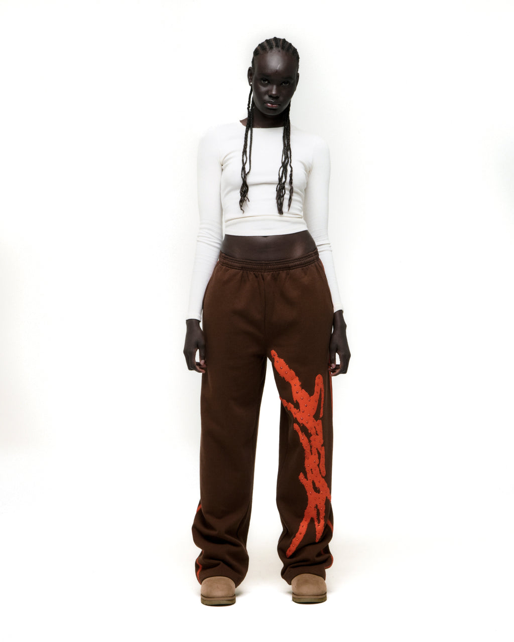 Brown cotton fleece wide-leg sweatpants with orange rhinestone "SP5DER" logo and sprayed side stripe.