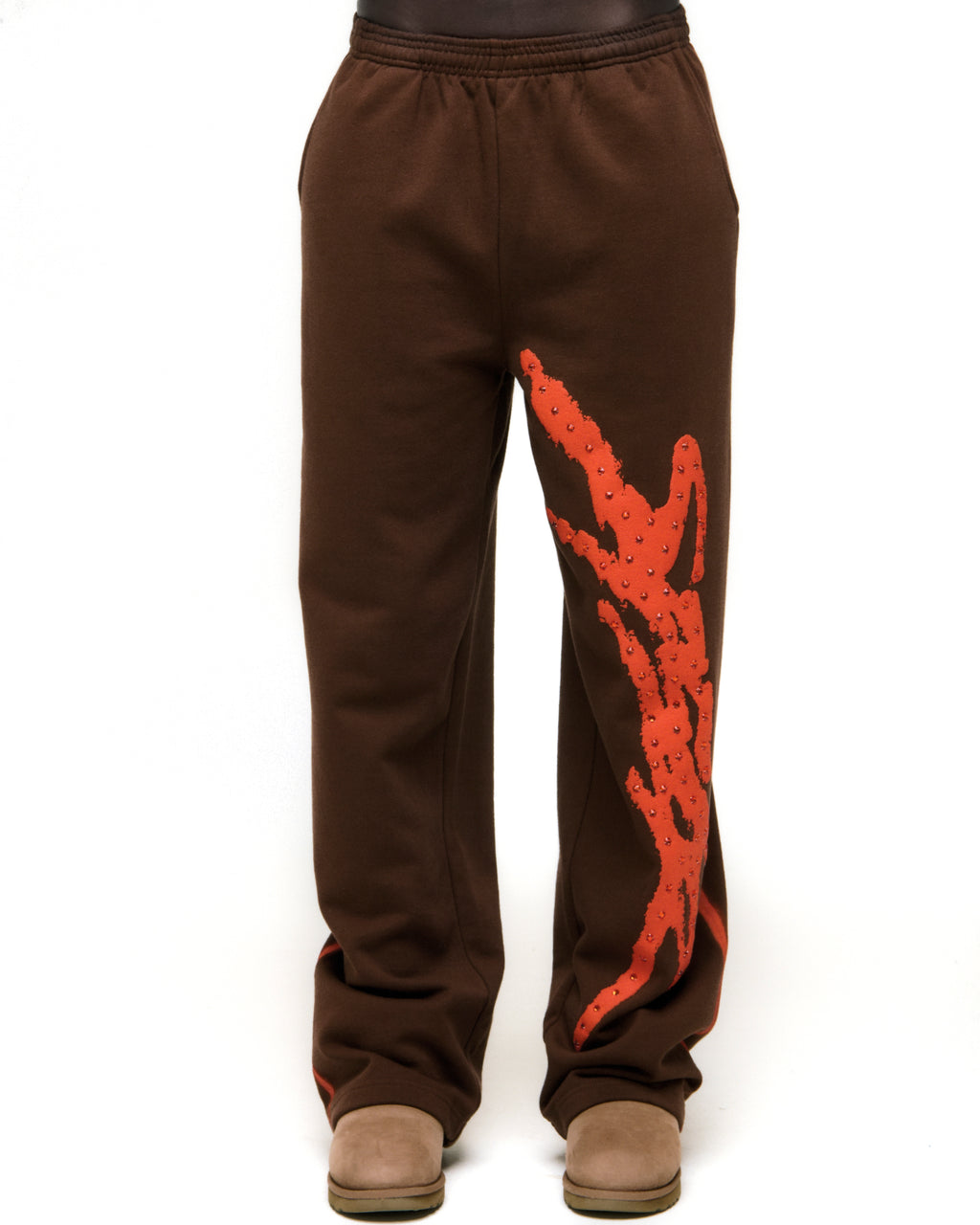 Brown cotton fleece sweatpants with orange SP5DER logo, rhinestone accents, and sprayed-effect side stripe.