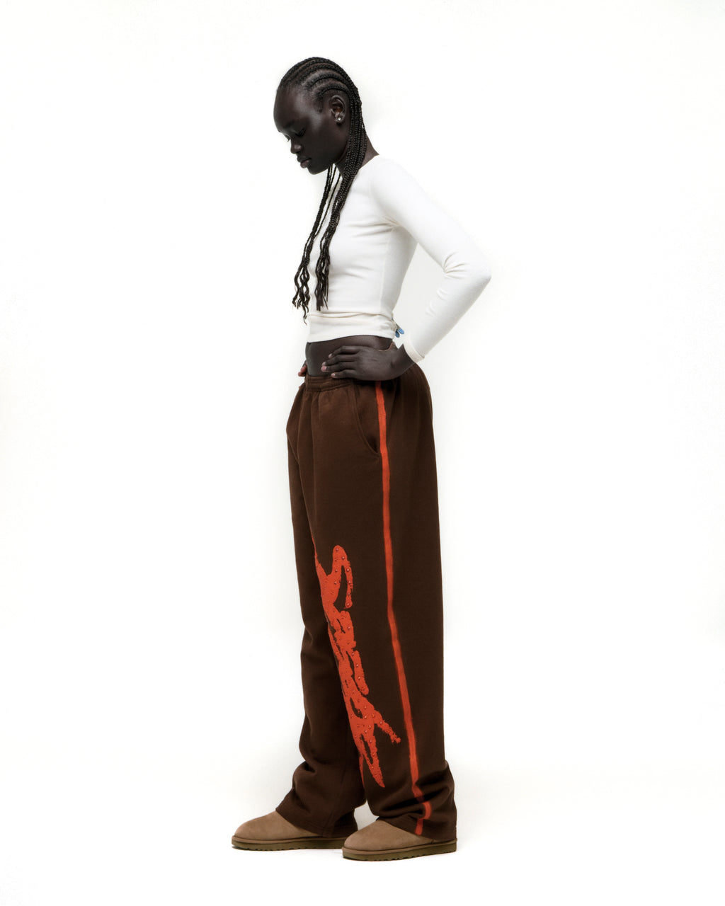 Brown cotton fleece sweatpants with "SP5DER" rhinestone logo and sprayed orange side stripe.