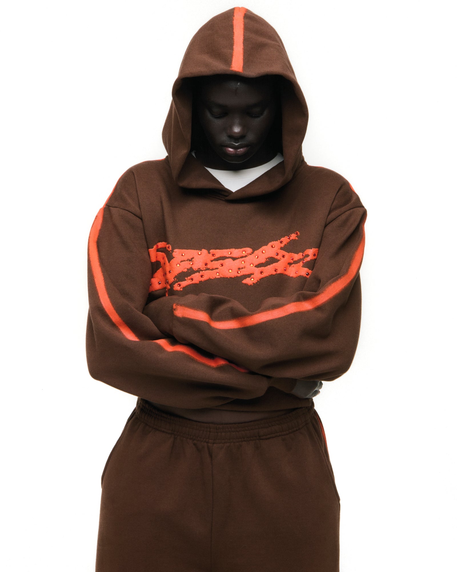 Brown cotton fleece hoodie with "SP5DER" logo and rhinestones, orange sprayed stripes on sleeves and hood.