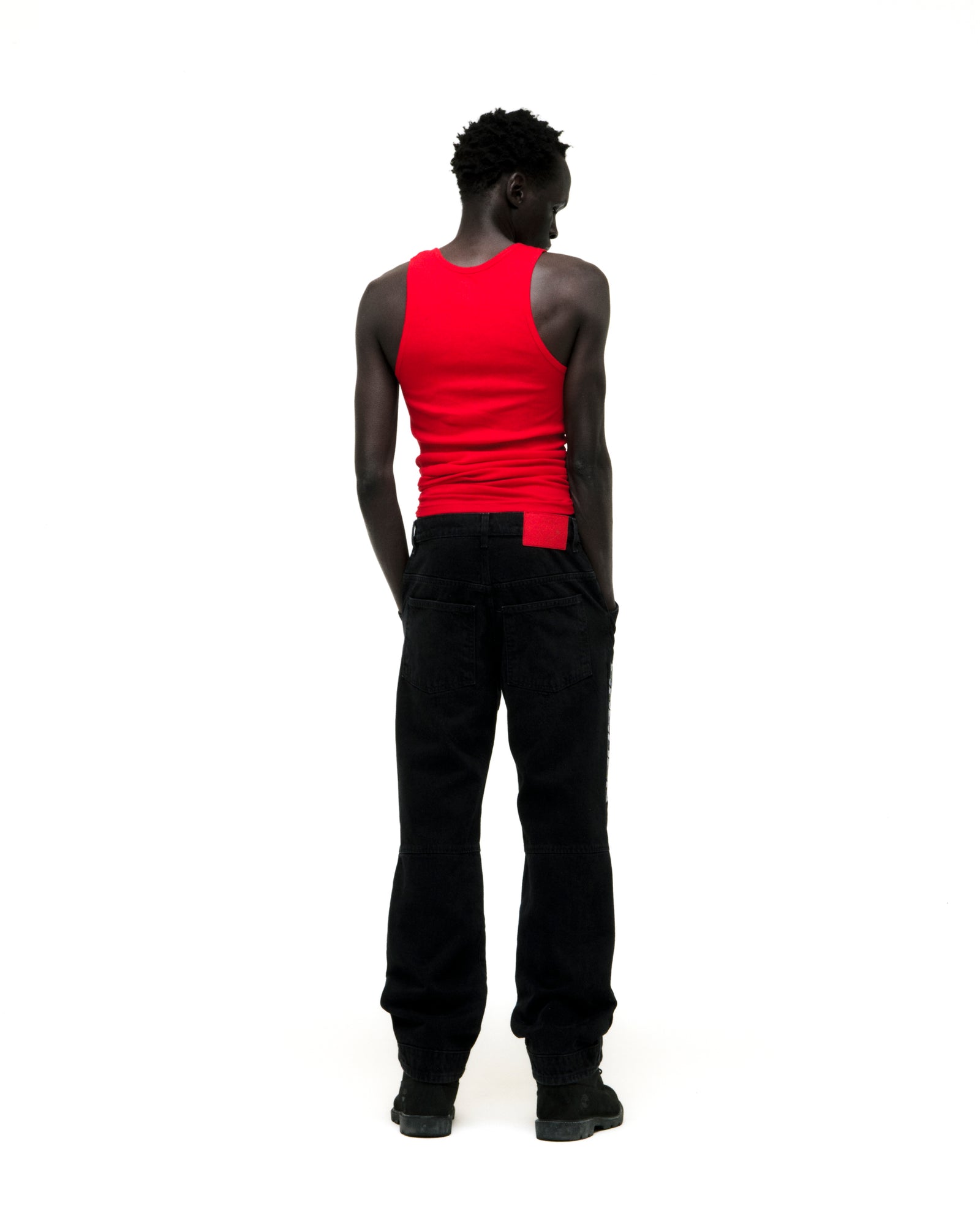 Man in faded black denim jeans with paneled knees, "SP5DER" logo, and distressed details.