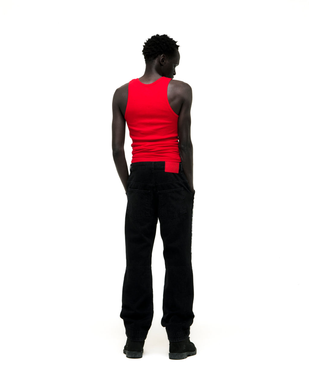 Man in faded black denim jeans with paneled knees, "SP5DER" logo, and distressed details.