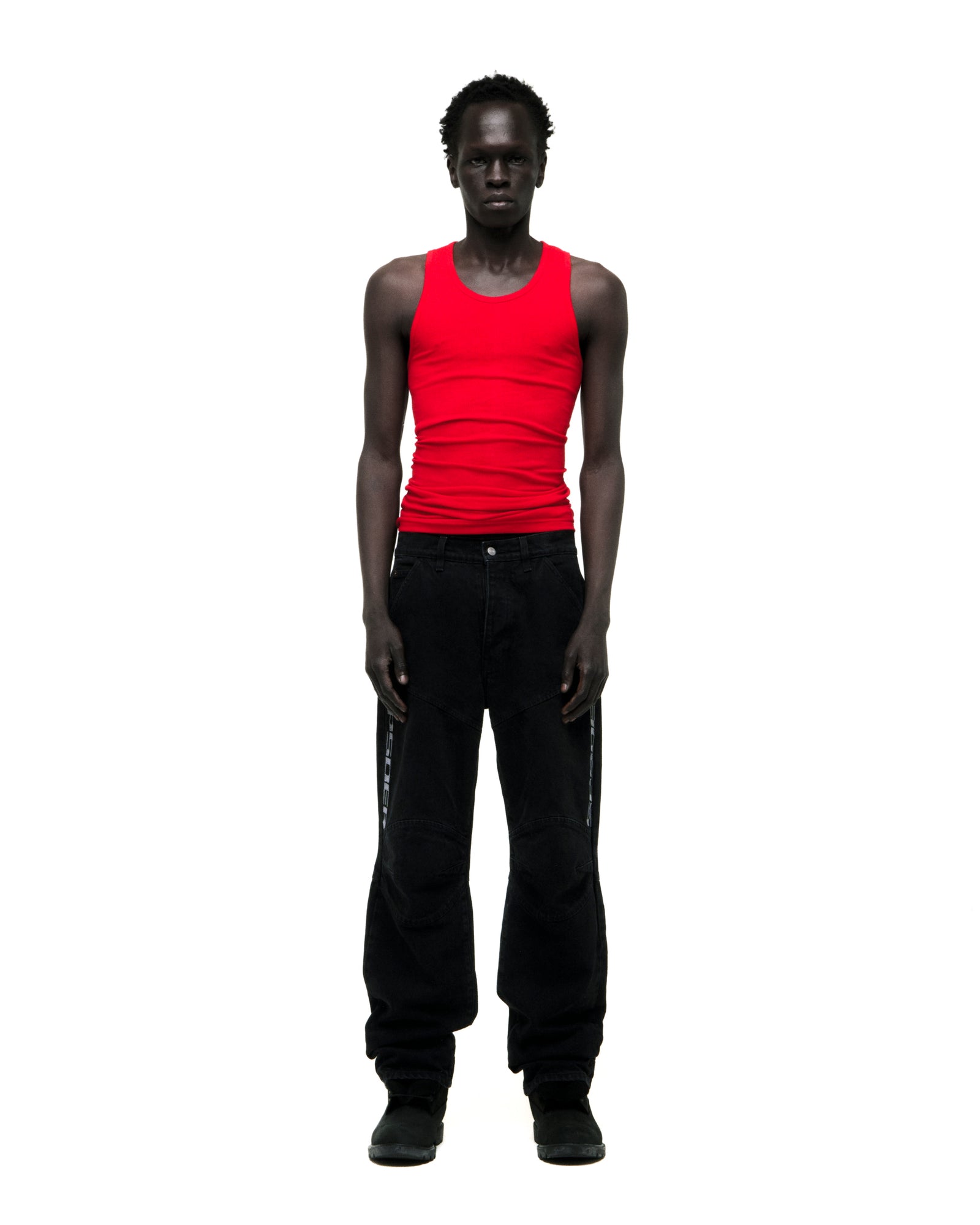 Man in black faded wash denim pants with "SP5DER" logo, paneled knees, and distressed details.