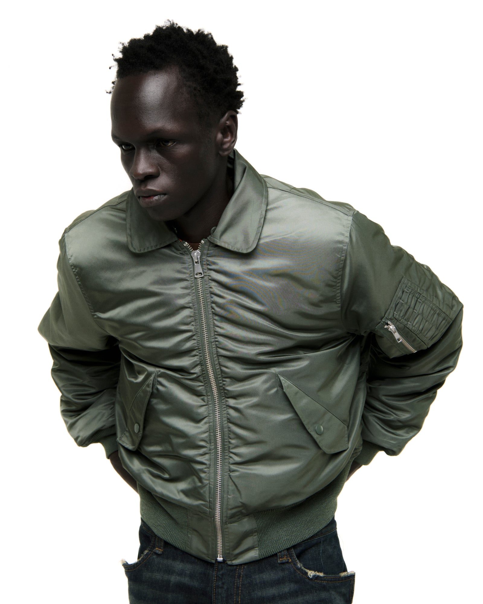 Man in an olive green nylon bomber flight jacket with front zip, snap pockets, and ribbed trim.