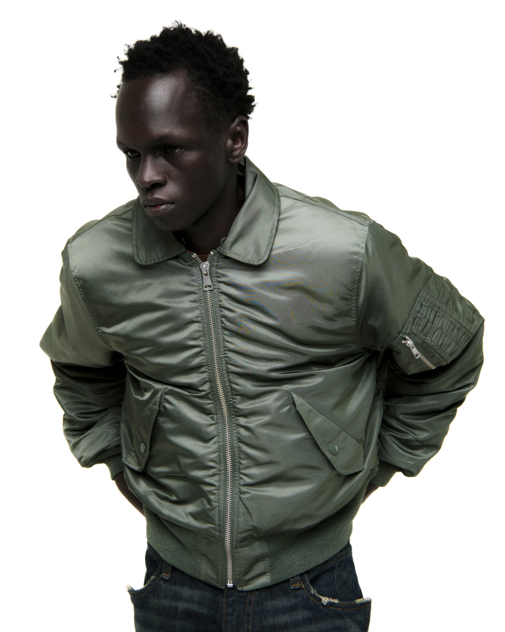 Man in an olive green nylon bomber flight jacket with front zip, snap pockets, and ribbed trim.