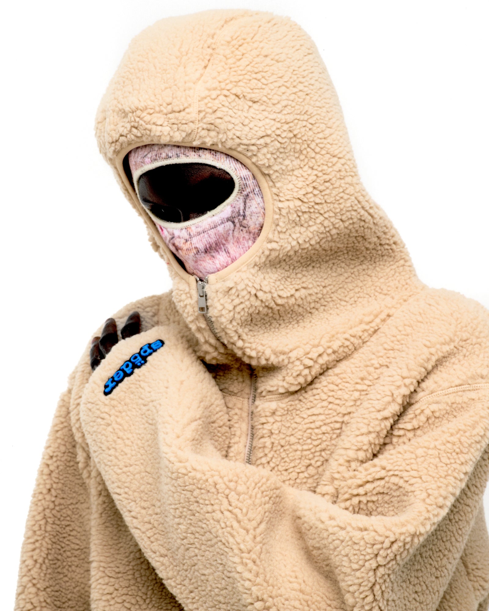 Beige sherpa fleece hooded zip-up jacket with a rubberized logo patch on the wrist.