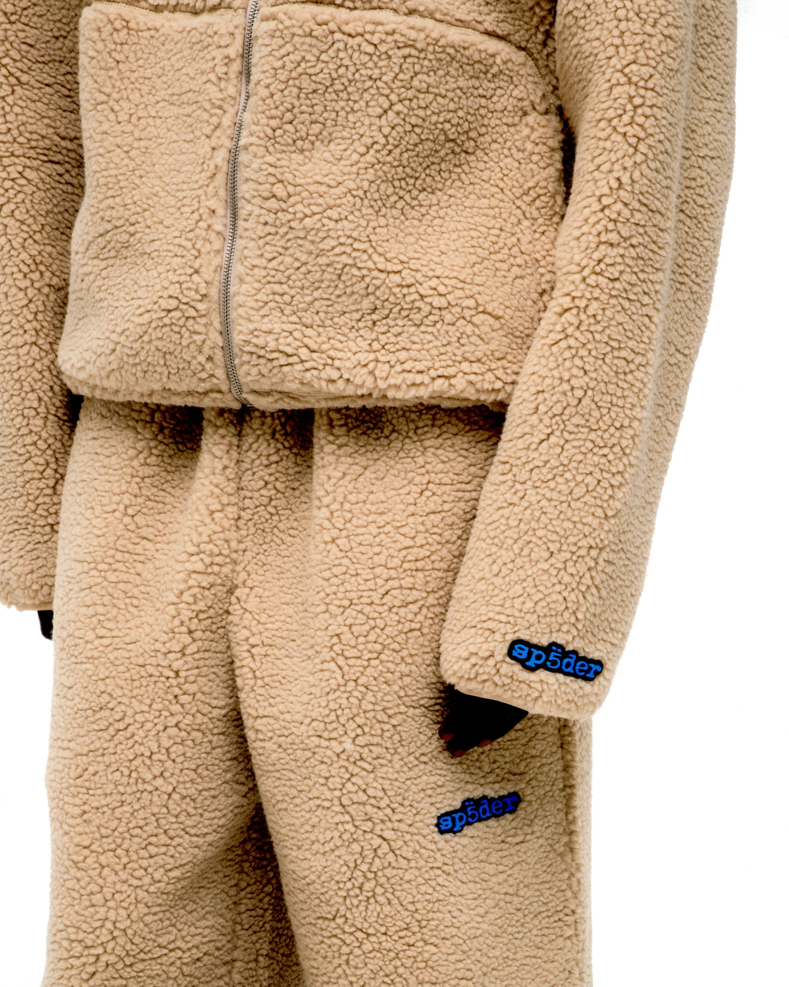 Beige teddy fleece zip-up jacket and matching pants with blue "sp5der" logo on wrist and leg.
