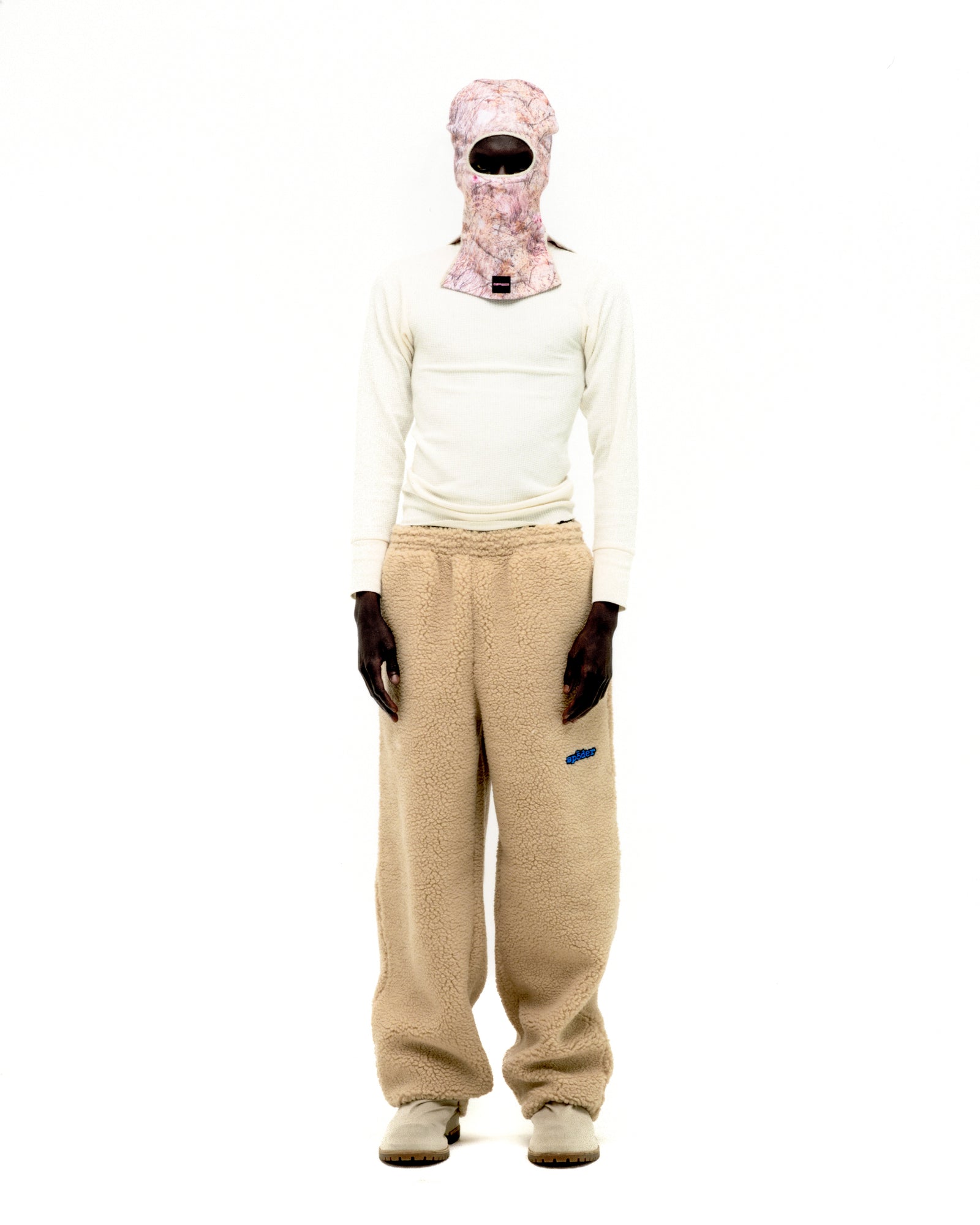 Beige teddy fleece pant with blue rubberized logo patch, worn by a model.