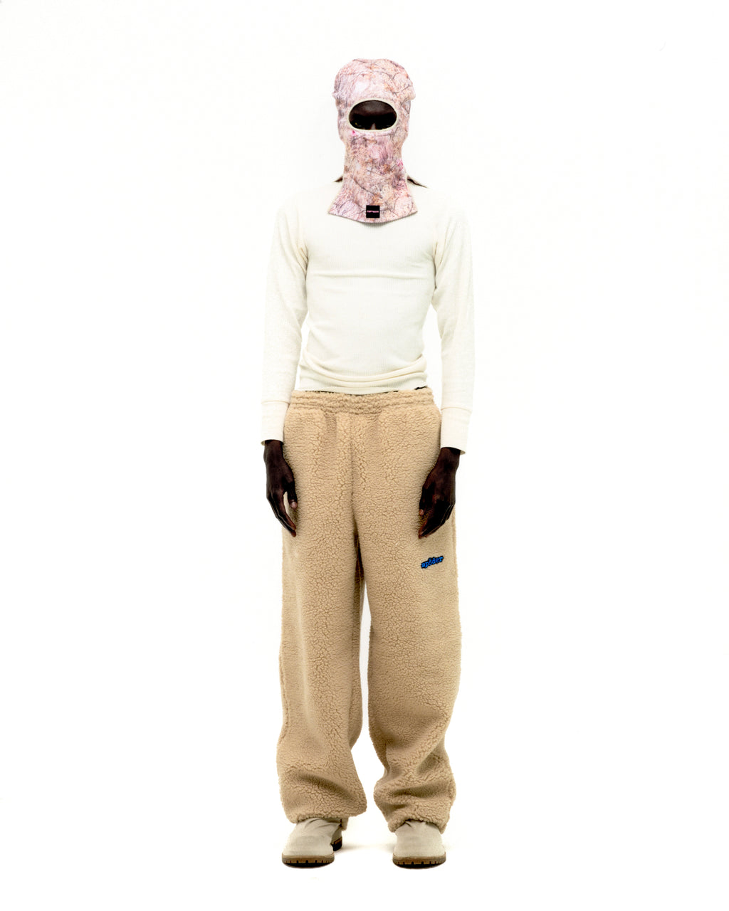 Beige teddy fleece pant with blue rubberized logo patch, worn by a model.