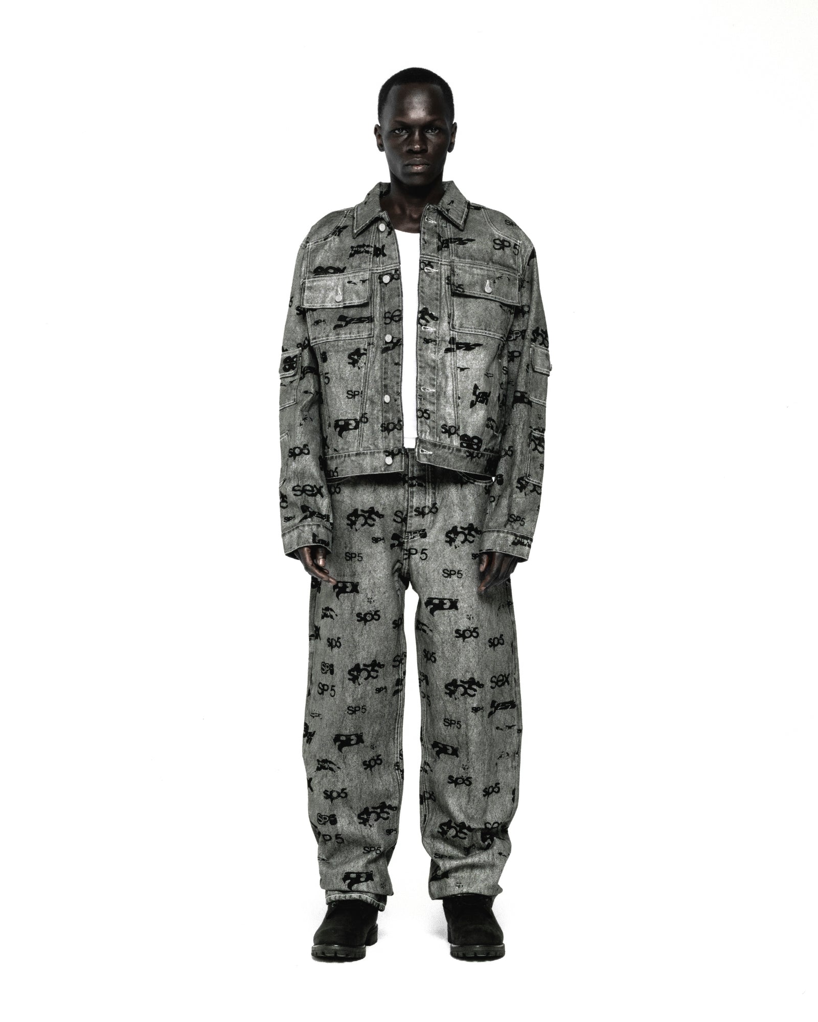 Model wearing a grey denim trucker jacket and matching pants with an all-over black print.