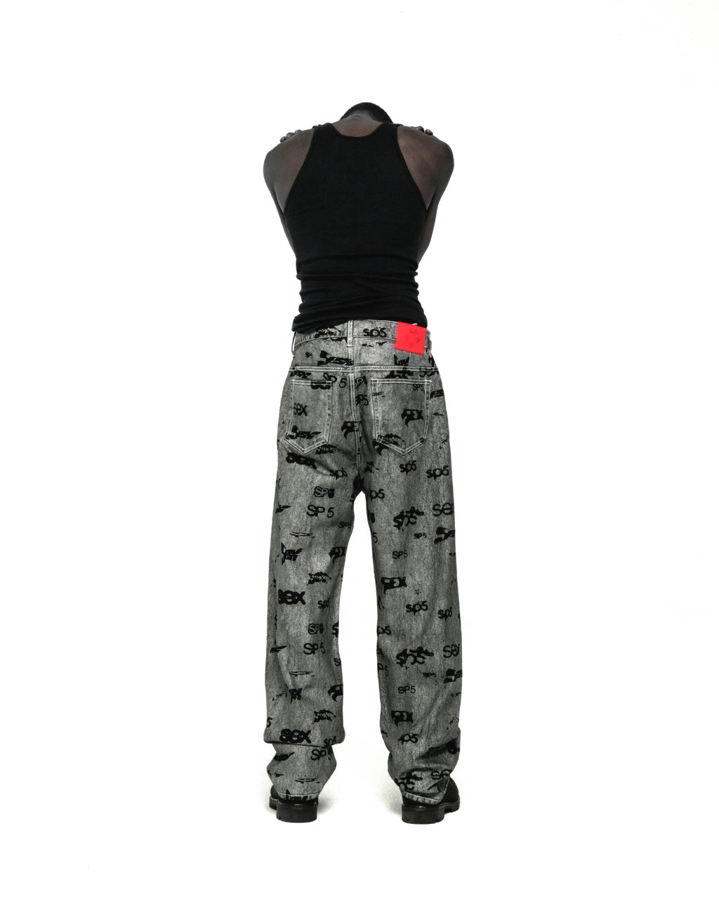 Gray denim pants with all-over black "SEX" and "SP5DER" print, red leather patch, and straight leg fit.