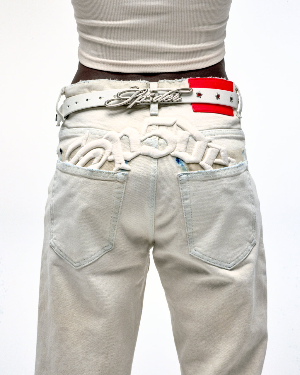 White leather R-05 Script Belt with cursive SP5DER buckle, studded star grommets, and silver tip.