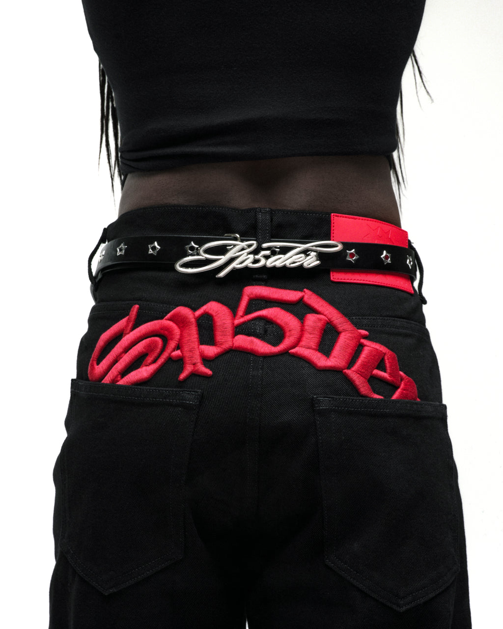 Black leather belt with silver cursive SP5DER buckle, studded star grommets, and silver tip.
