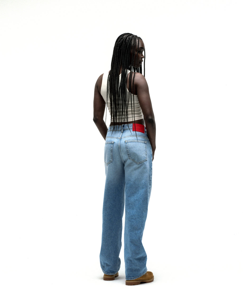 Model wearing vintage wash distressed logo denim jeans with a red back patch and straight leg fit.