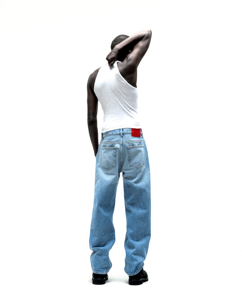 Man in vintage wash, straight leg denim jeans with a red branded leather back patch.