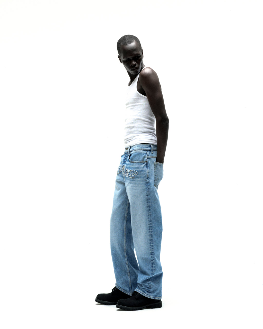 Man in vintage wash distressed logo V3 denim jeans with frayed "SP5DER" embroidery.
