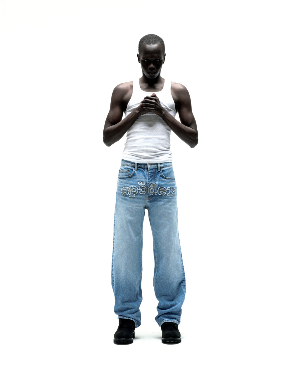Man in vintage wash distressed logo V3 denim jeans with frayed "SP5DER" embroidery.
