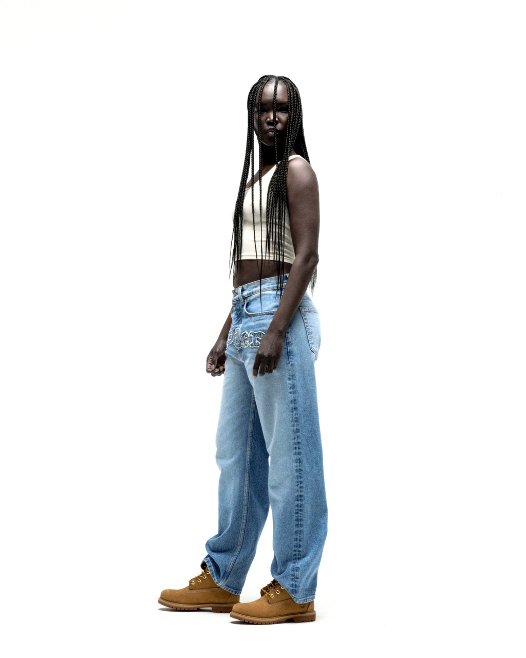 Model wearing vintage wash distressed logo V3 denim jeans with frayed "SP5DER" embroidery.
