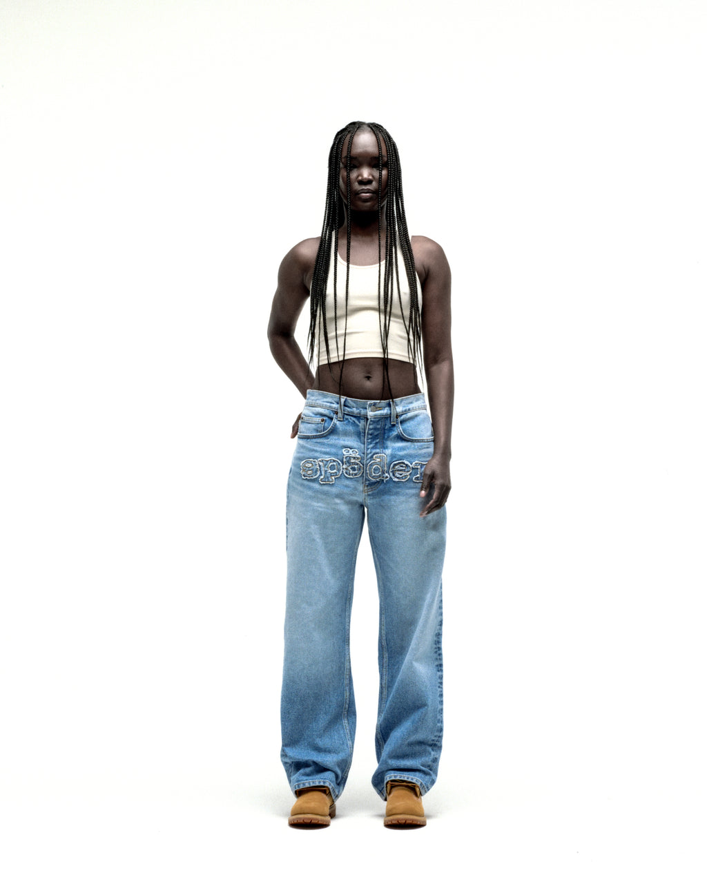 Model wearing vintage wash, straight leg denim jeans with frayed "SP5DER" logo across the crotch.