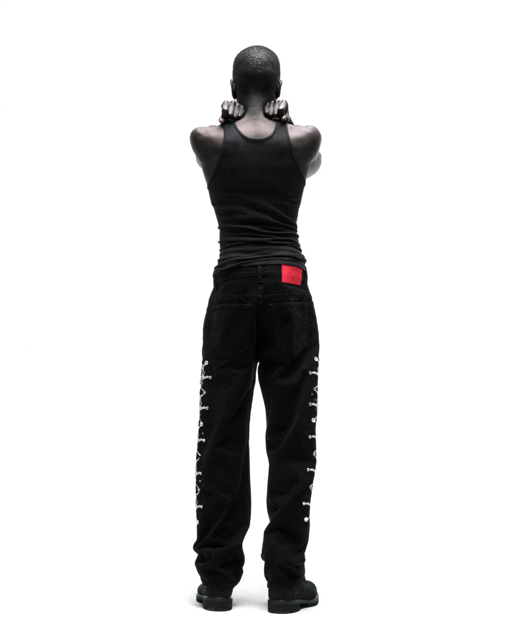 Black vintage wash denim pants with web print and rhinestone embellishments down both legs, worn by a person from behind.