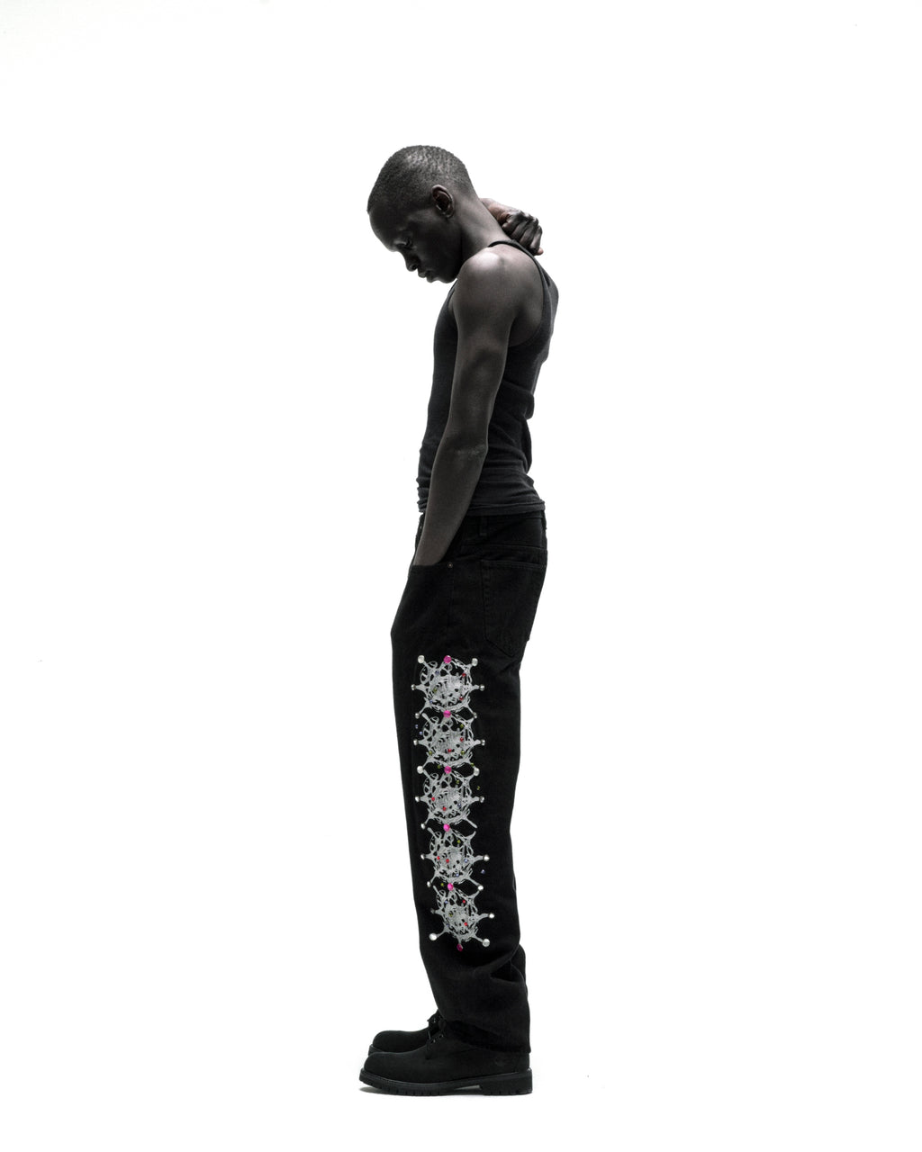 Black vintage wash denim pants with web print and rhinestone embellishments down the leg, worn by a man.