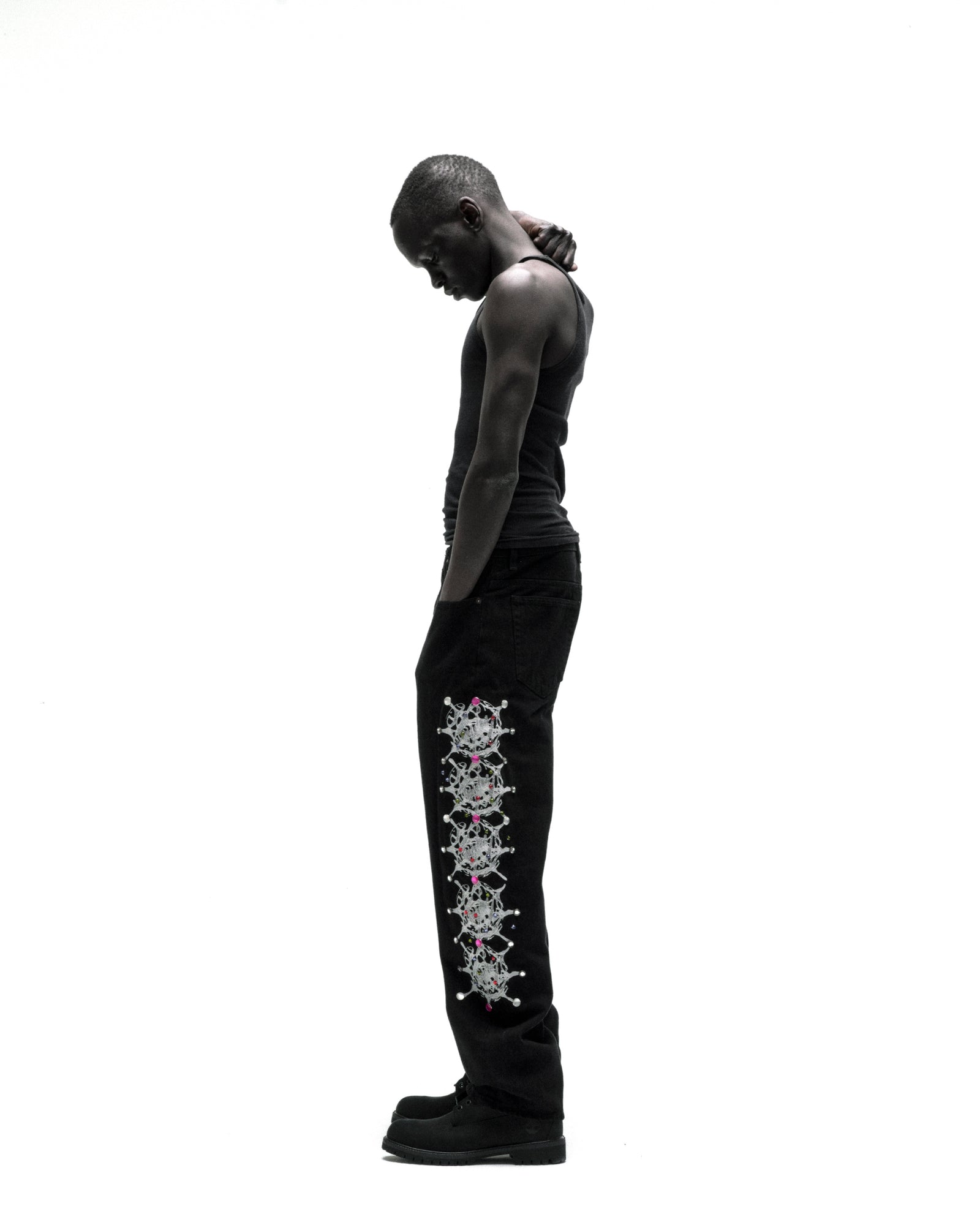 Black vintage wash denim pants with web print and rhinestone embellishments down the leg, worn by a man.