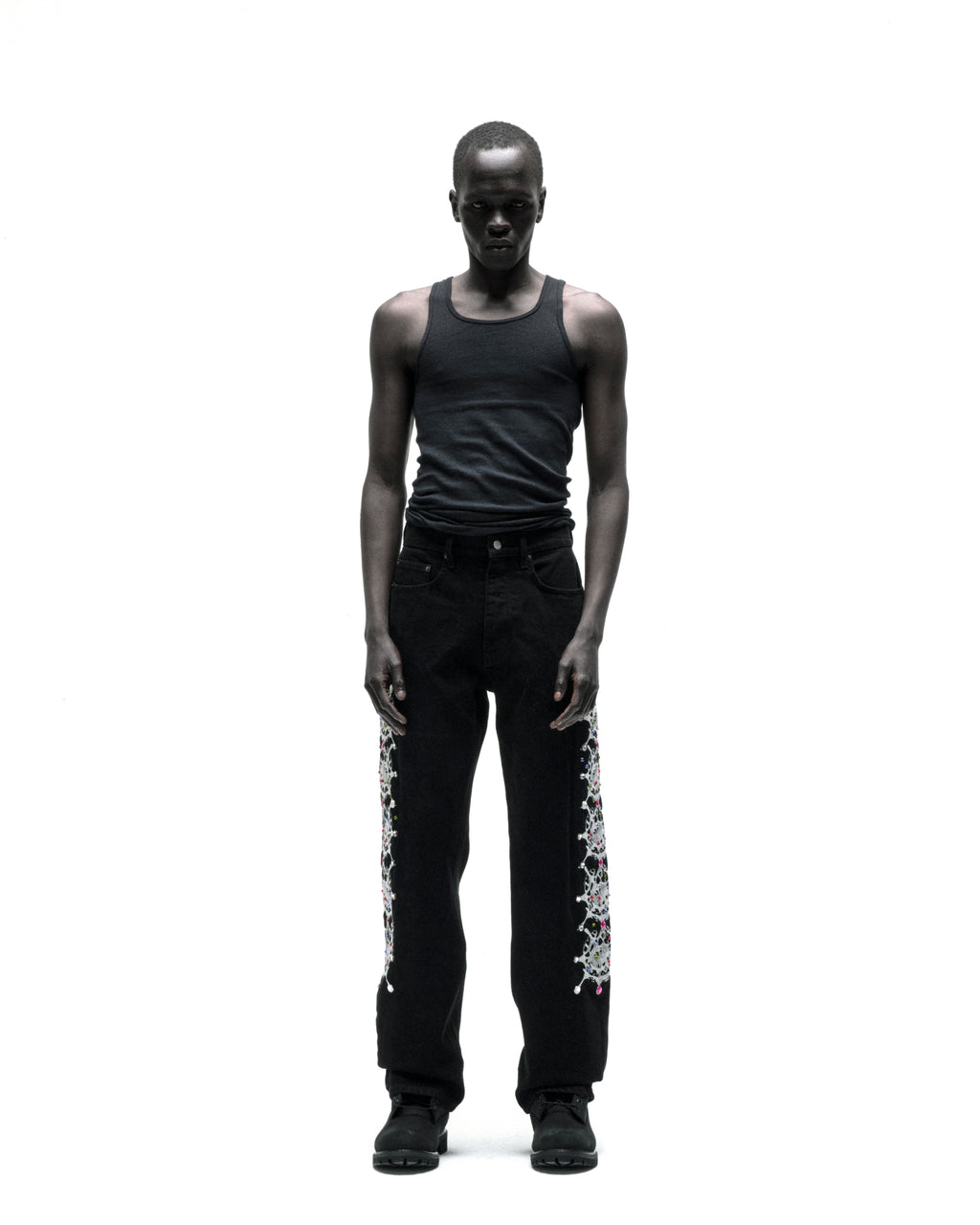 Man wearing vintage wash black denim pants with web print and rhinestone embellishments down both legs.