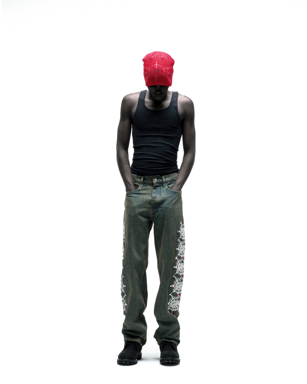 Man in vintage wash denim pants with web print and rhinestone embellishments, black tank top, and red bandana.