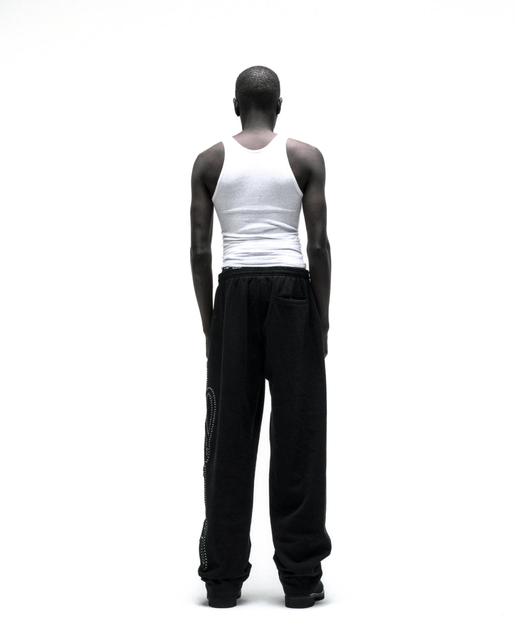 Black wide-leg cotton fleece sweatpants with rhinestone script down the leg, seen from behind.