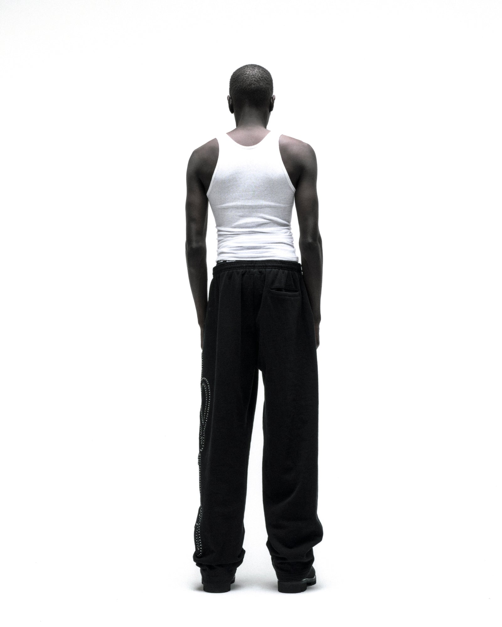 Black wide-leg cotton fleece sweatpants with rhinestone script down the leg, seen from behind.