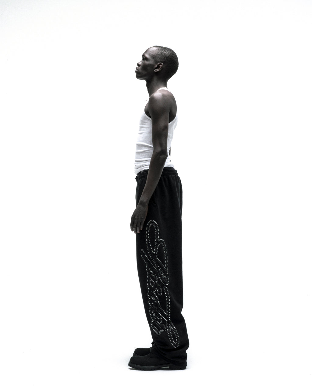Black wide-leg sweatpants with rhinestone script down the leg, worn by a model in profile.