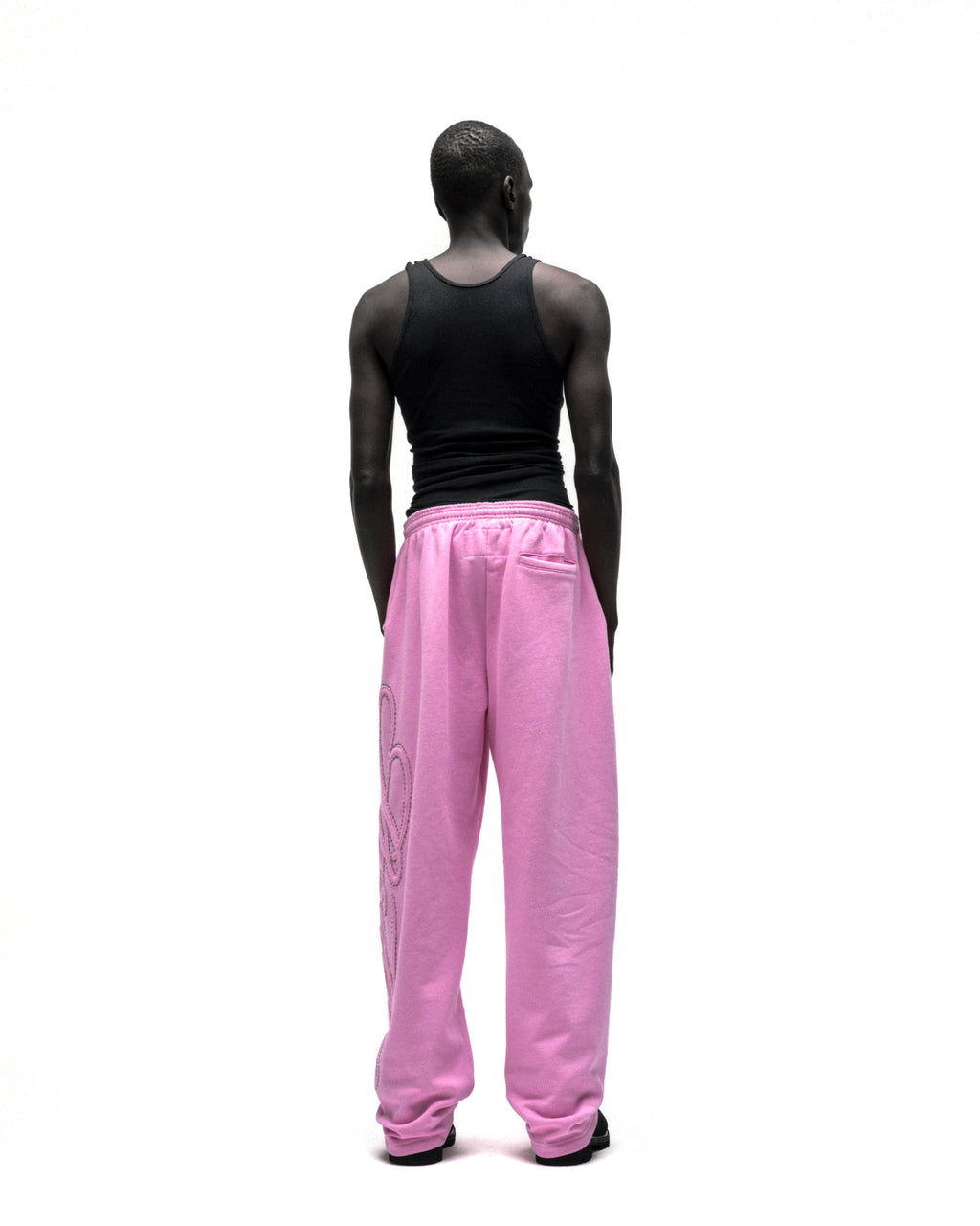 Rear view of a person wearing pink wide-leg sweatpants with rhinestone script design down the leg.