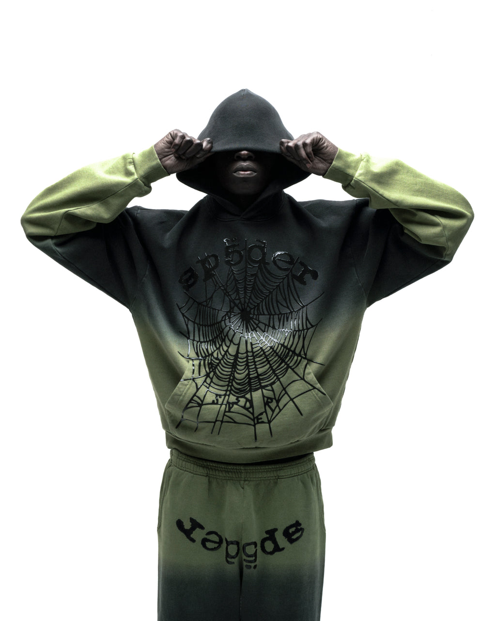 Model wearing an OG Web Ombre Hoodie in black and green, featuring a spiderweb graphic and matching sweatpants.