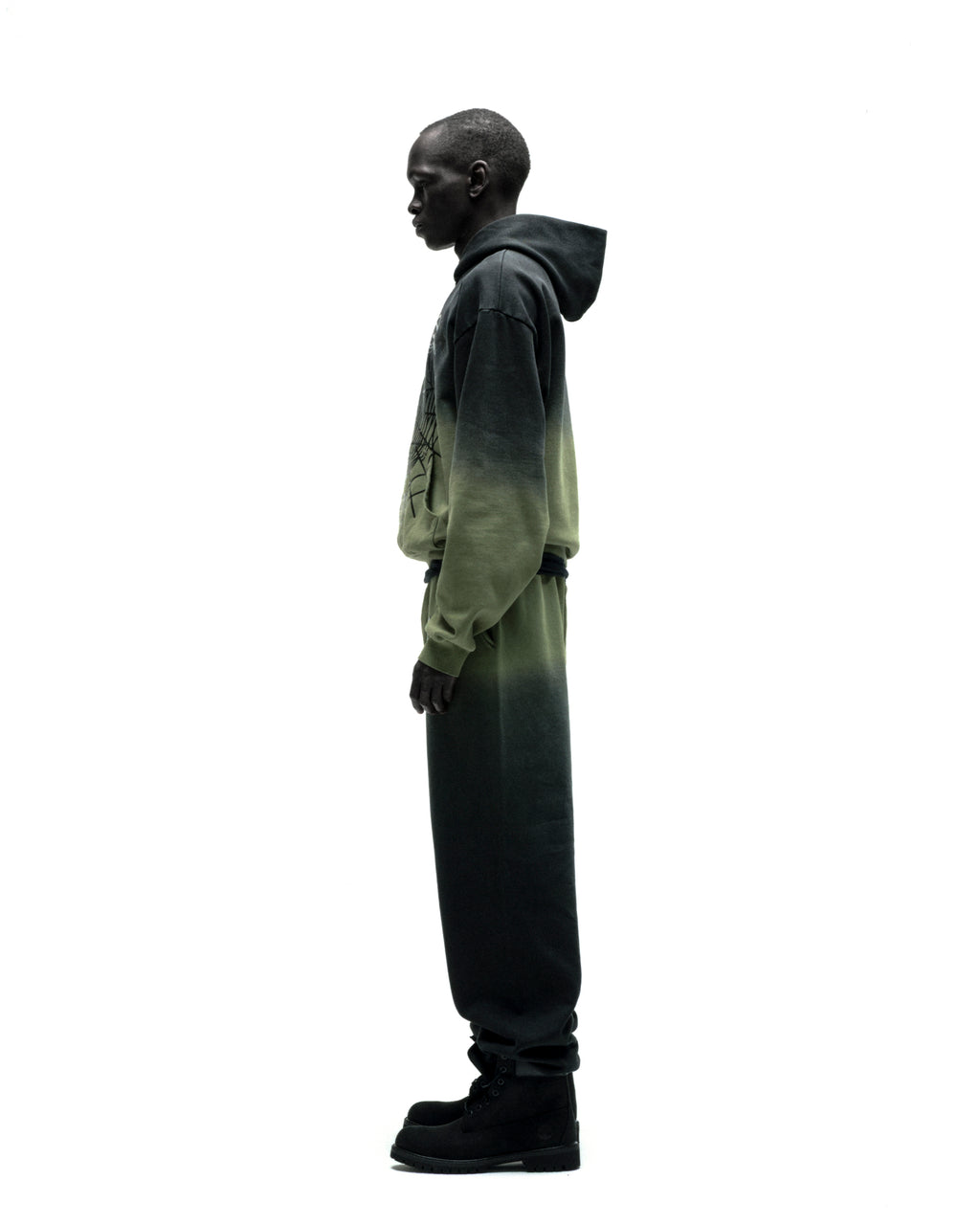 Man in OG Web Ombre Hoodie and sweatpants, fading from dark to light green, with a front graphic.