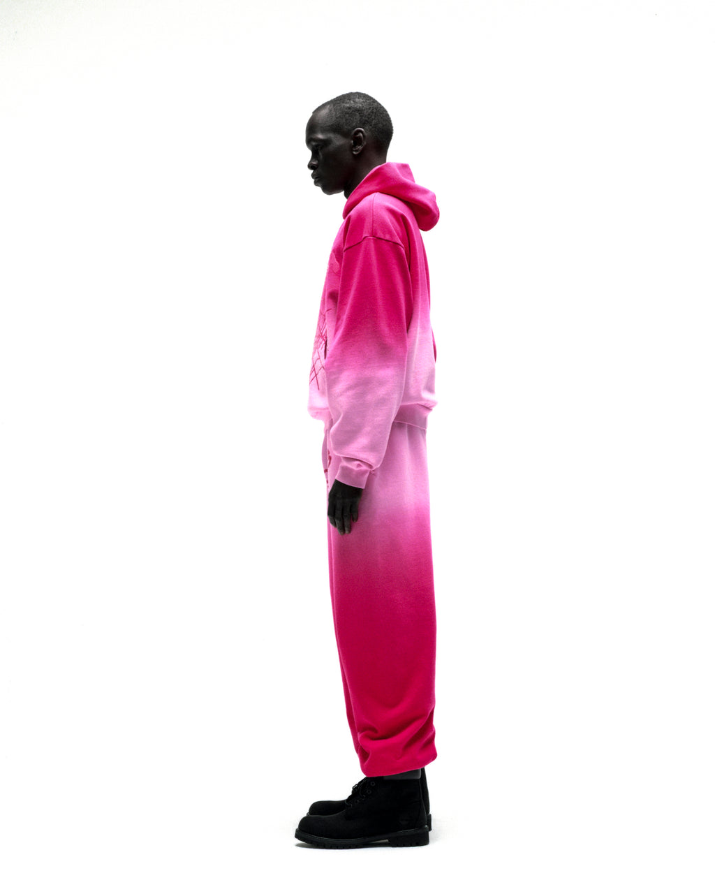 Man in an OG WEB Ombre Hoodie and sweatpants, fading from light to dark pink, with a web design.
