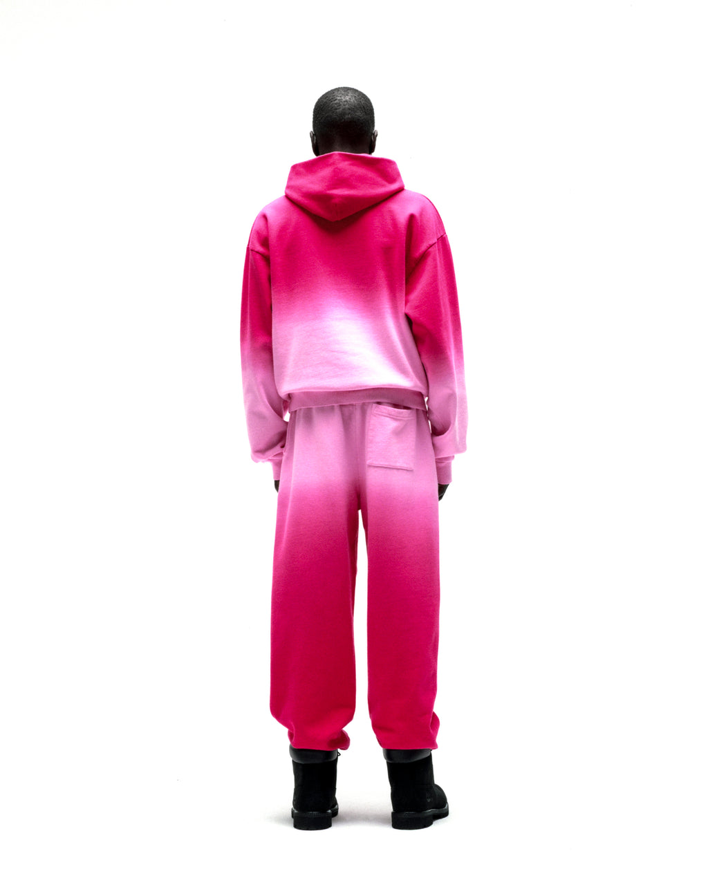 Back view of a model wearing an OG WEB OMBRE HOODIE and matching sweatpants, featuring a pink to white ombre design.
