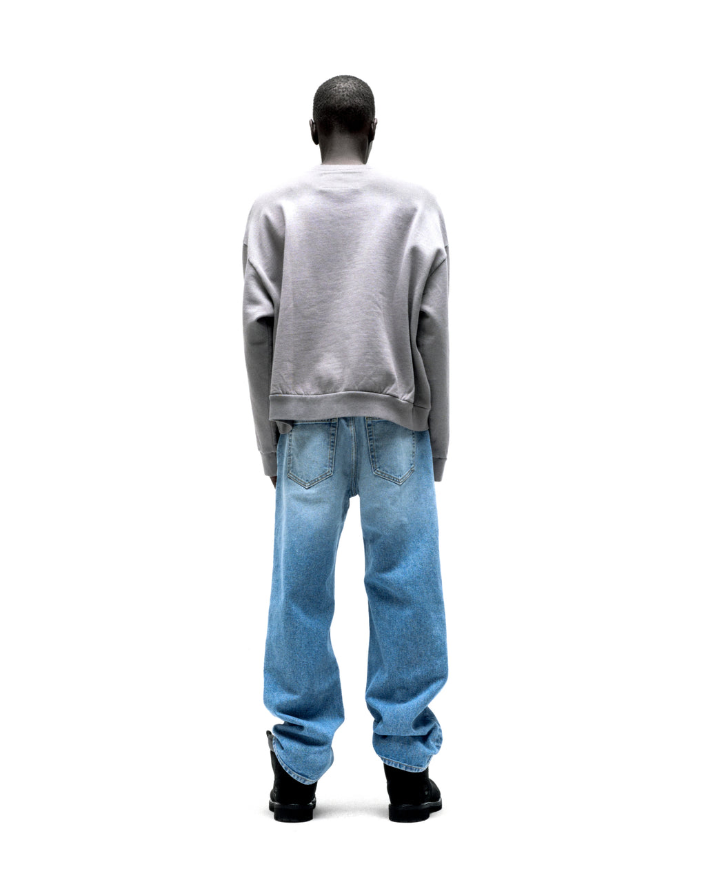 Model from behind wearing a grey SP5DER CUNTRY CREWNECK sweatshirt with blue jeans.